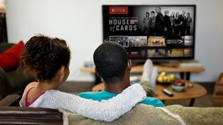 Ryggen af en mand og en kvinde, som sidder på en en sofa og ser Netflix på et tv