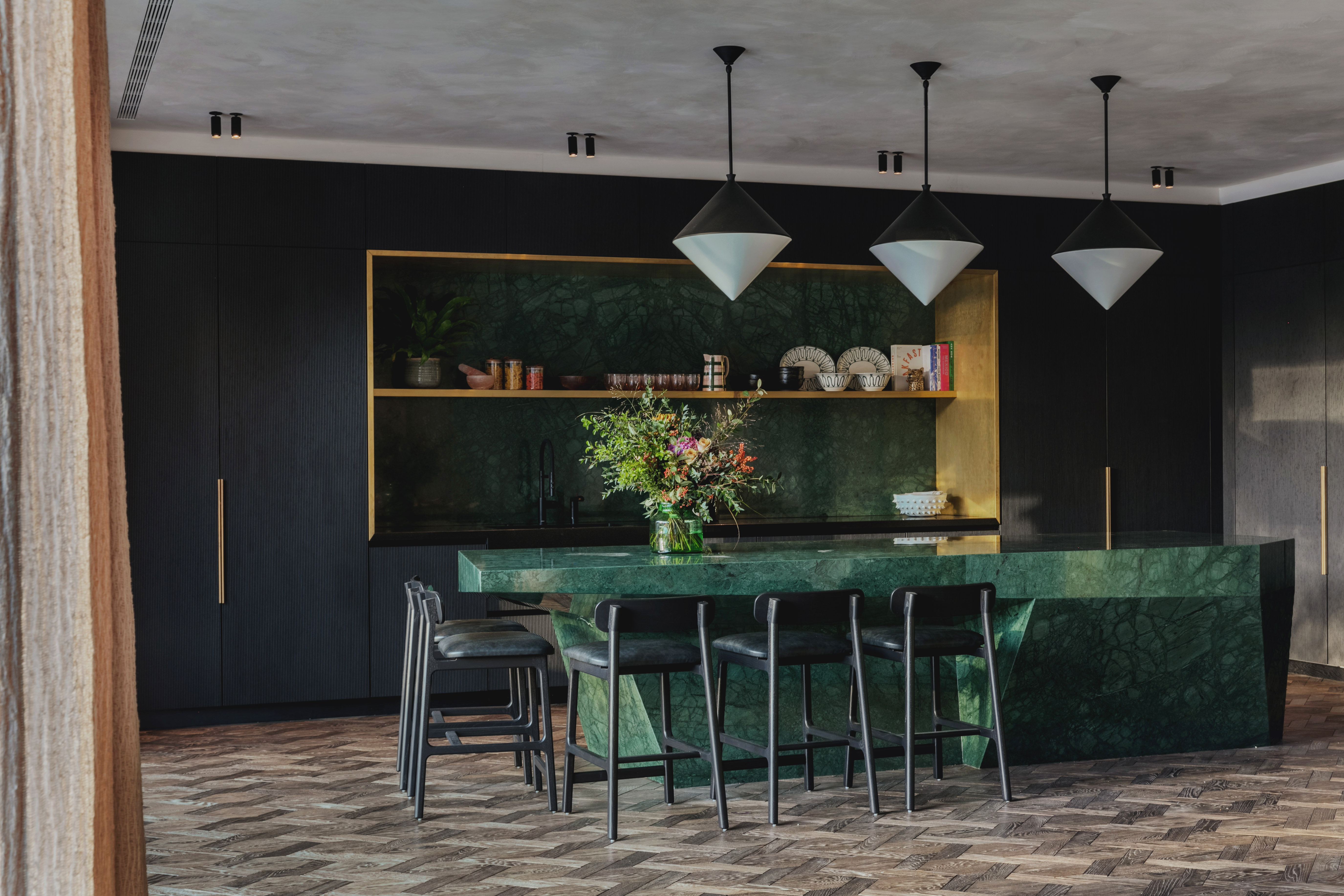 A kitchen with a large, green marble island with black chairs around it