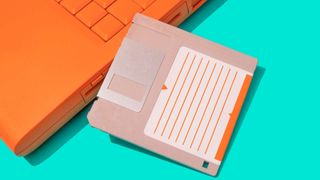 High angle close up view of orange laptop and a floppy disk on green background