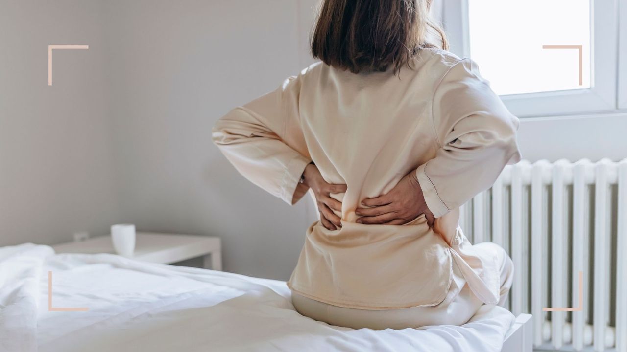 woman sat on bed facing window with hands on back