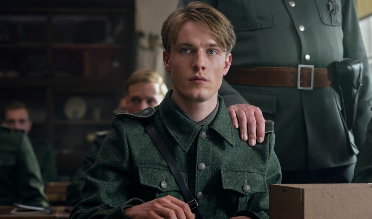 Werner sitter iklädd uniform vid ett bord i Netflix-serien Ljuset vi inte ser.