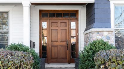 wooden front door with landscaping and paneling