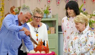 Great British Baking Show Paul cuts a cake while Prue, Sandi, and Noel watch