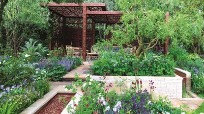 A brown wooden pergoda in a wild garden with raised flower beds and trees