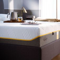 The Tempur Sensation Elite mattress on a bed with a breakfast tray and newspaper with reading glasses on top