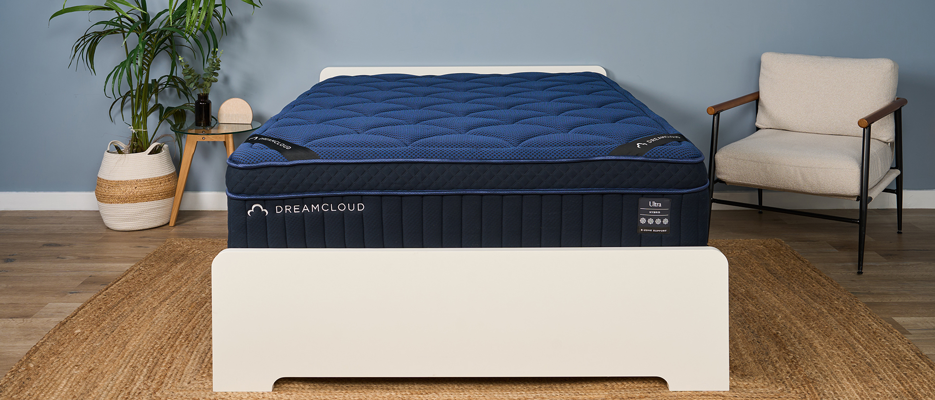 The image shows a navy blue mattress on a white bedframe, set within a muted blue bedroom