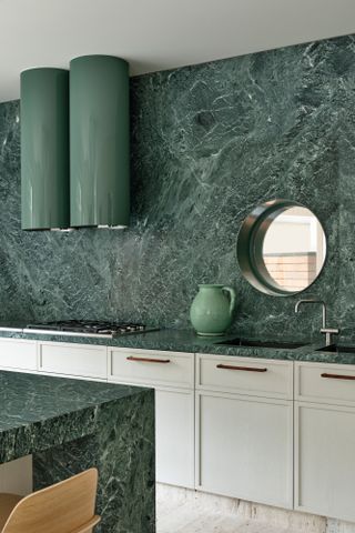 White kitchen with green stone units and walls and porthole window looking to outside