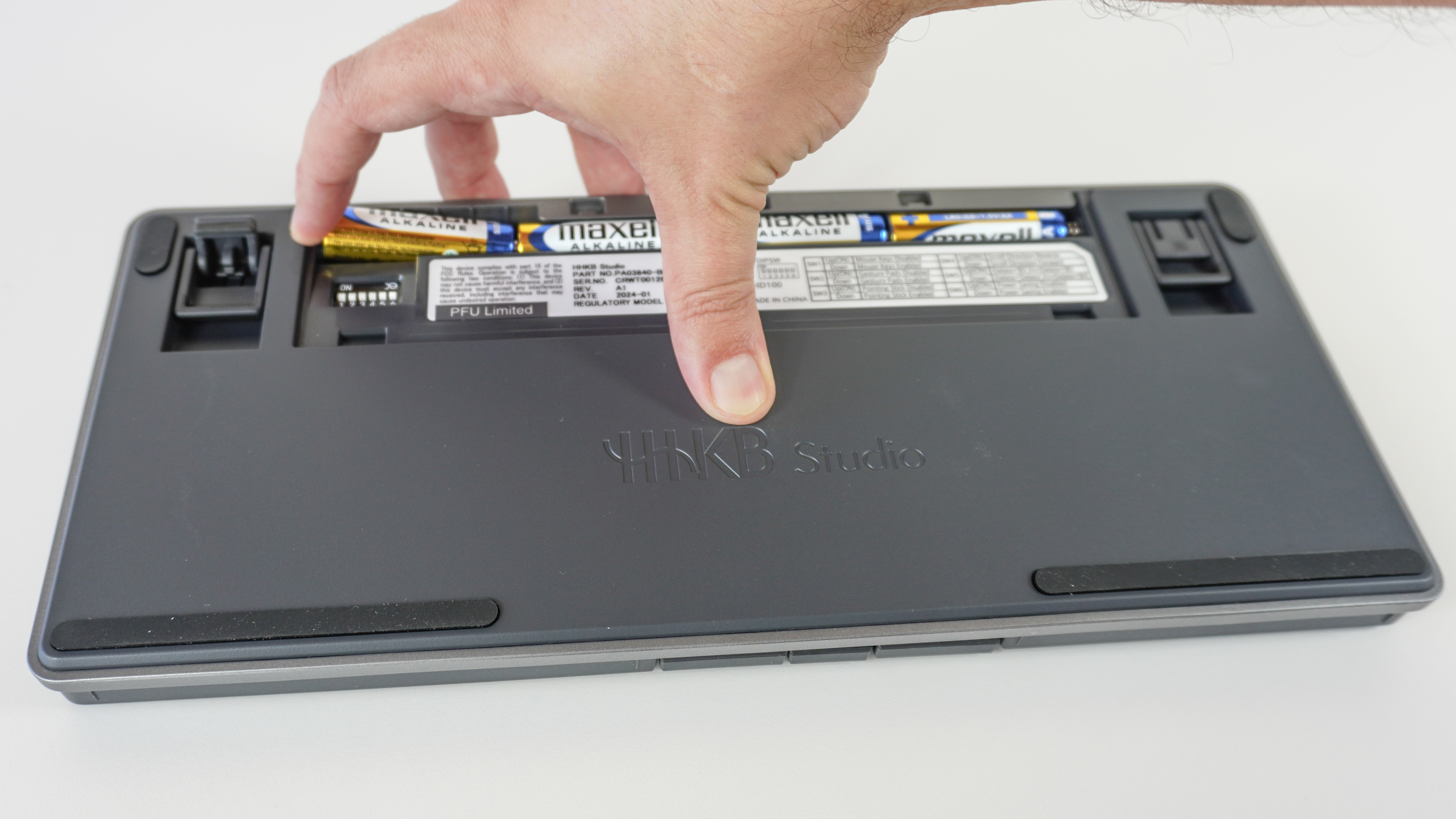 A person loading AA batteries into the back of the HHKB Studio