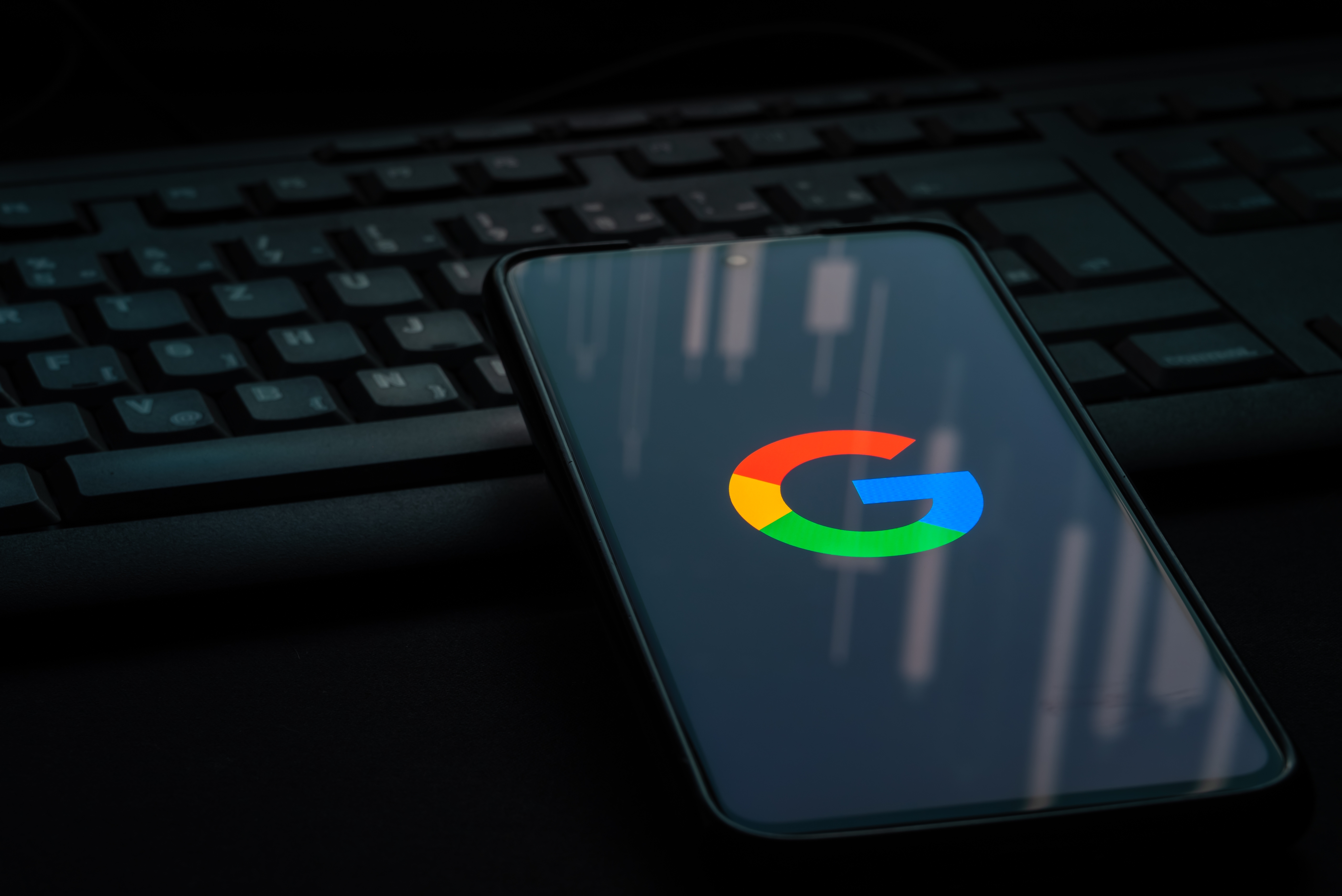 Google logo on smartphone screen laying on computer keyboard