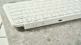the top of a a white wireless bluetooth keyboard resting on a clean white table showing its charging port and mac/windows switch