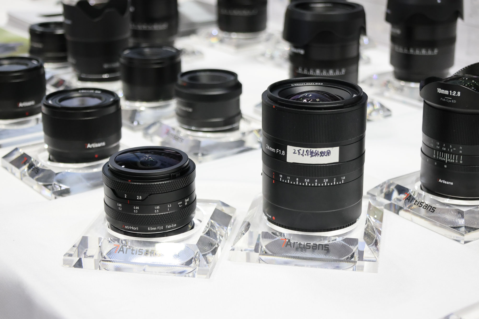 Array of 7Artisans lenses on a white display table at CP+ 2025 photography show.