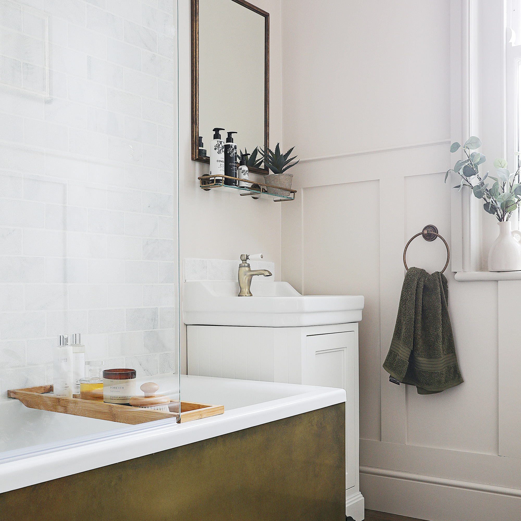 bathroom with cream panelled walls compact sink unit and bath with brass panell