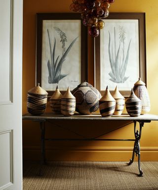 A hallway carpet idea with yellow walls, woven natural carpet and rattan baskets on the entry table