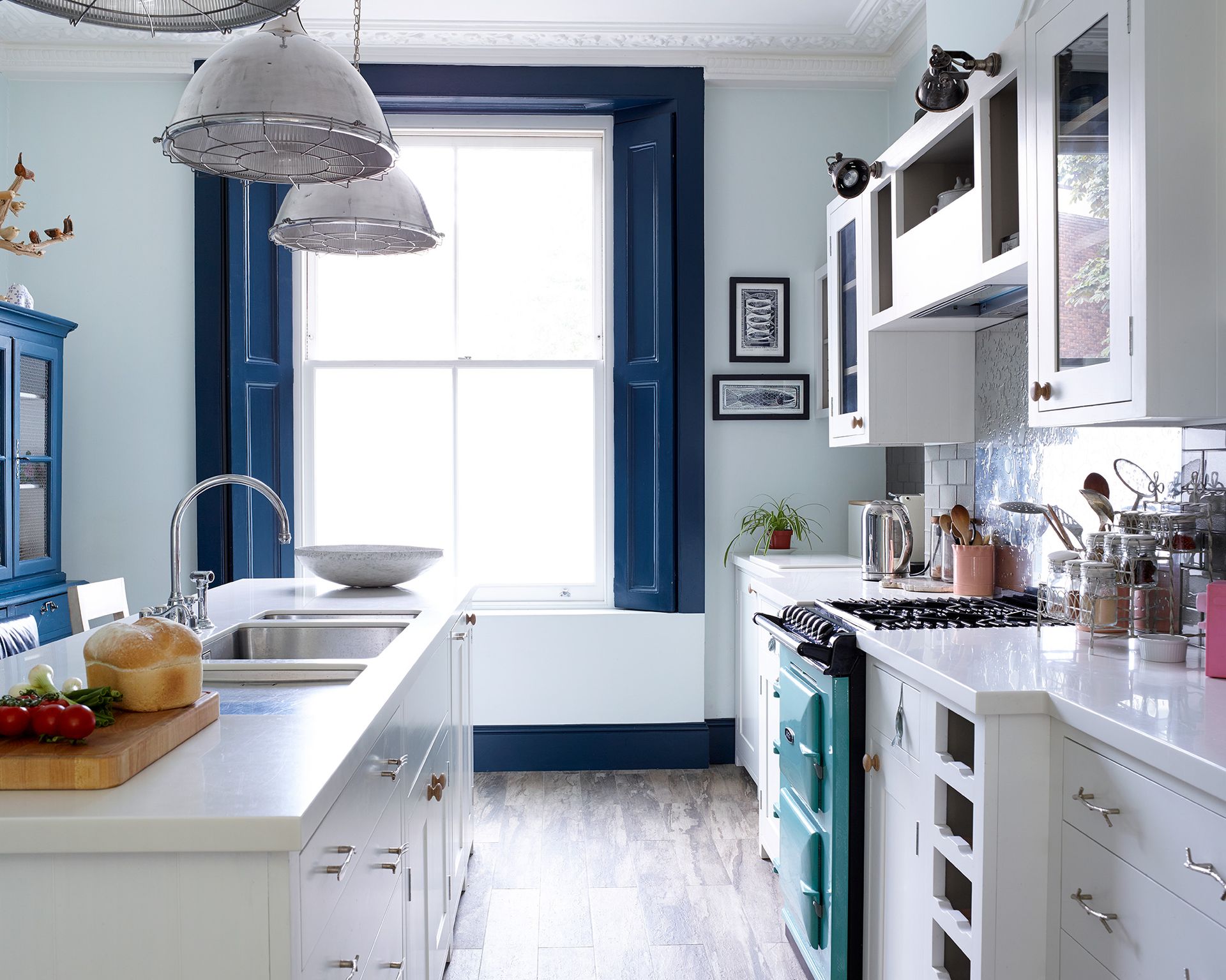 A kitchen with white cabinets and worktops and a large window with dark blue shutters