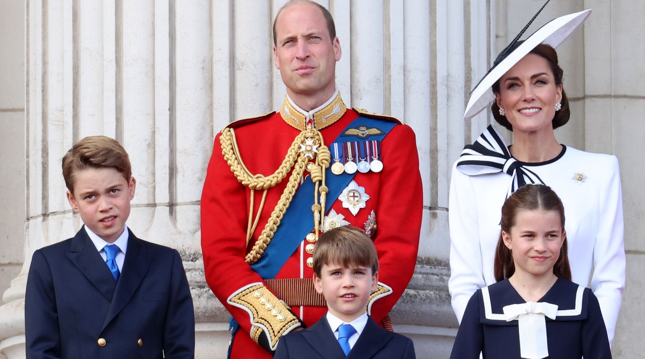 Prince William wears military uniform, Kate Middleton wears a white dress with navy detailing and a matching hat, Prince George and Prince Louis wear matching suits, and Princess Charlotte wears a navy and white nautical-inspired dress