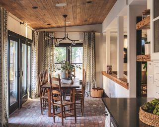 dining area with wooden ceiling, statement pendant, wooden table and chairs, black metal doors and brick floor