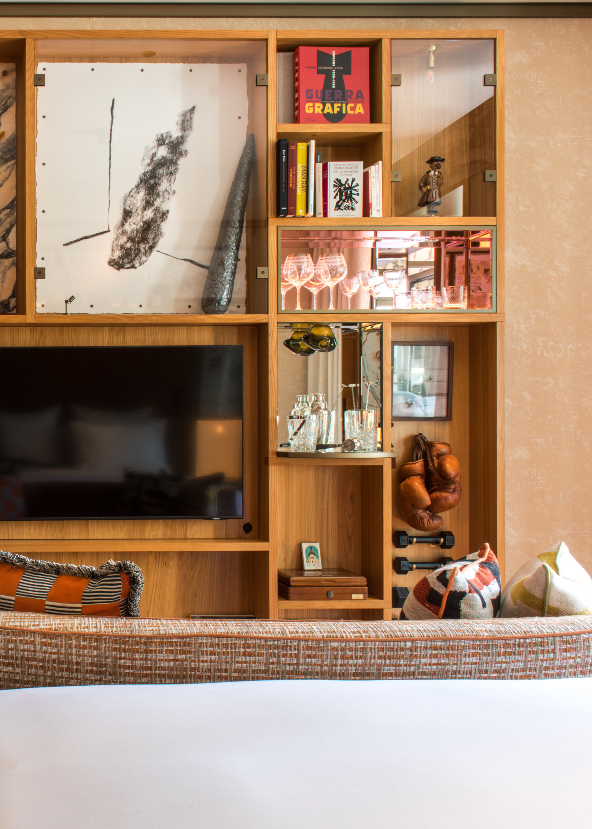 A wood wall unit with a bar setup and a set of books alongside a set of weights and boxing gloves