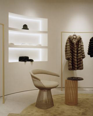 Interior design at Yves Salomon Conduit Street. showcasing white recessed 3-layered shelf, fur coats hanging on an hanging rail and a chair