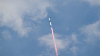 a large silver rocket flies through a blue sky above a column of flame