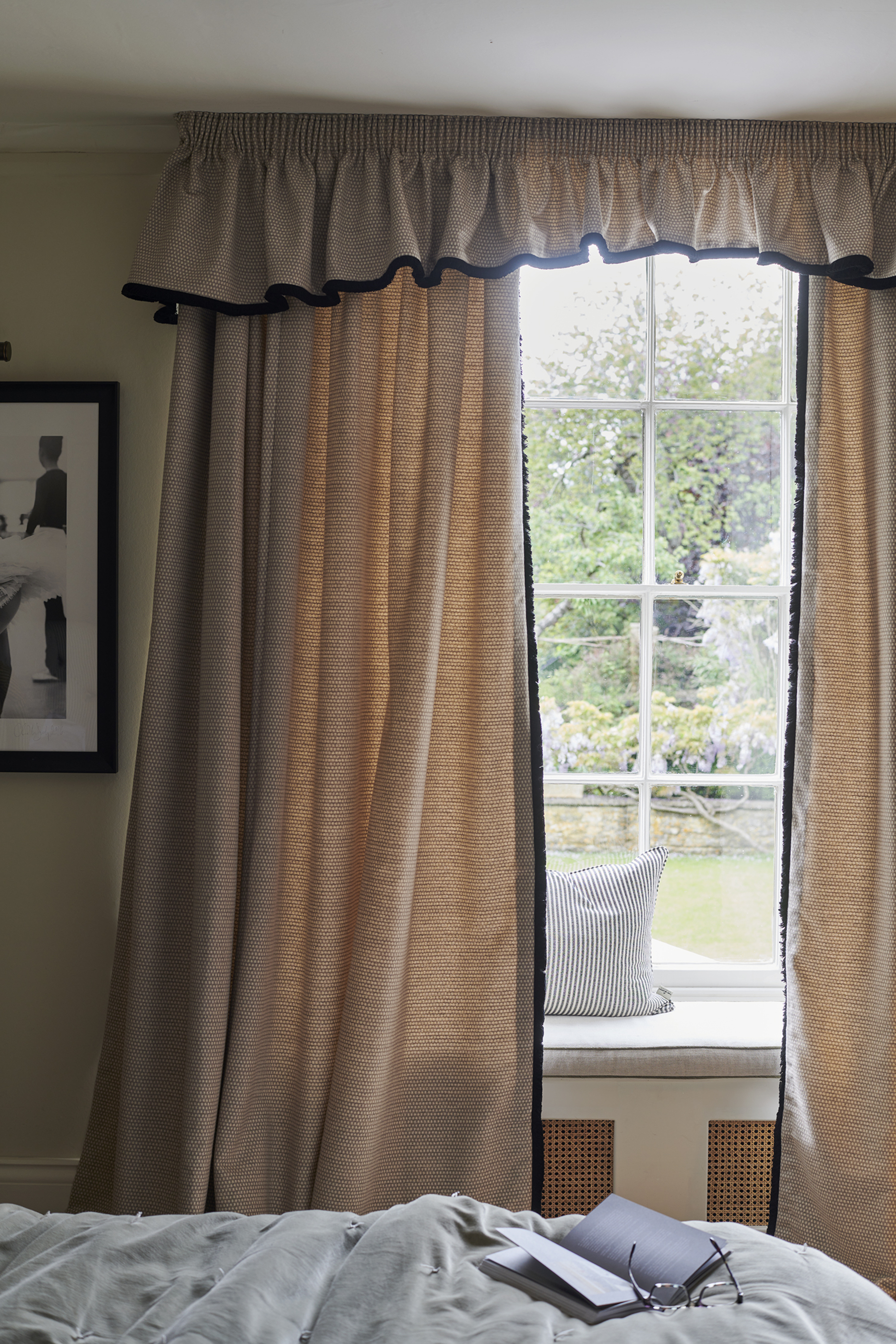 A bedroom with linen curtains with a pelmet and blue piping detail