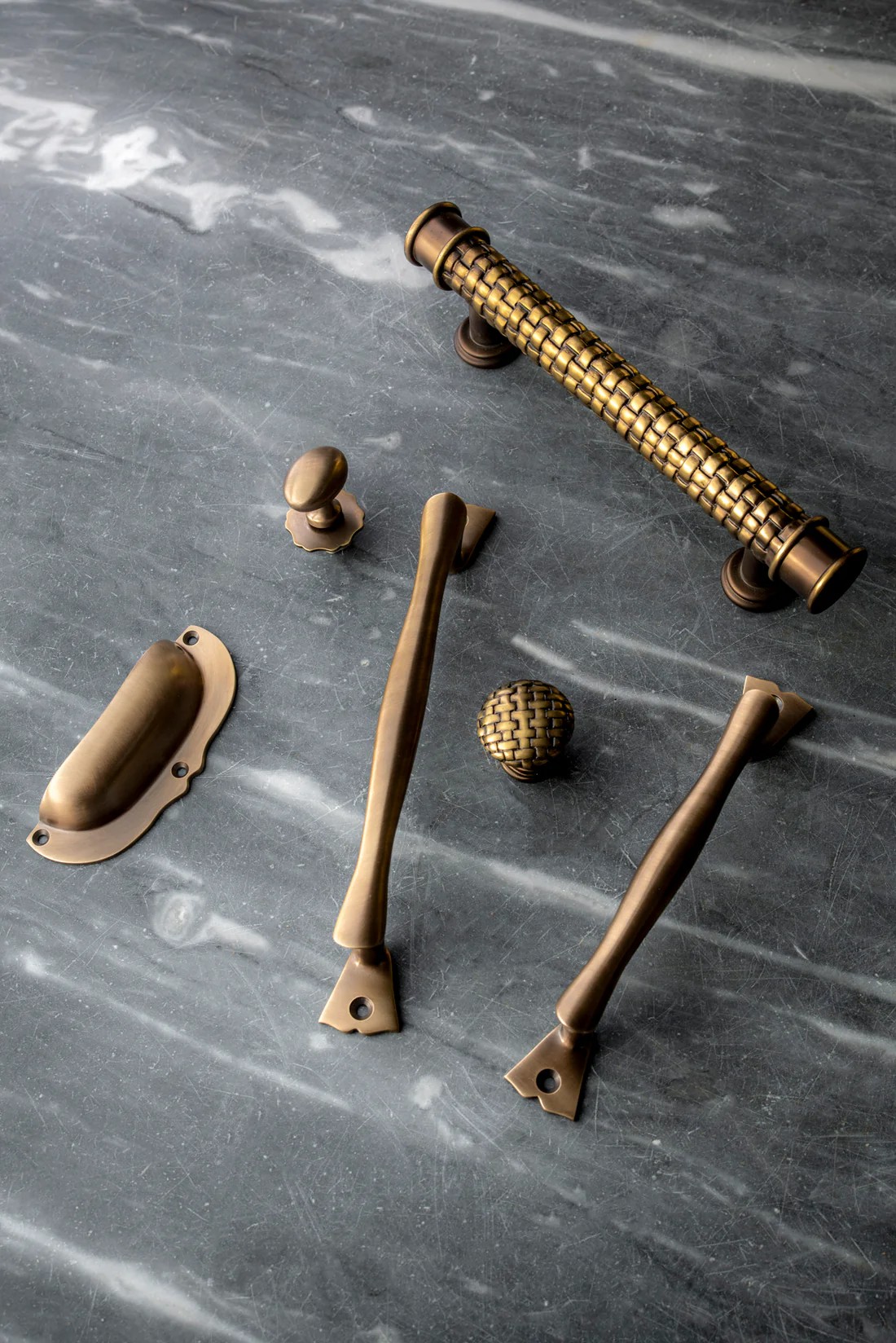 Image of a collection of brass cabinet hardware on a dark marble countertop.