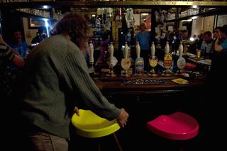 A view of the pub bard with people around the bar and a man about to lift a yellow bar stool