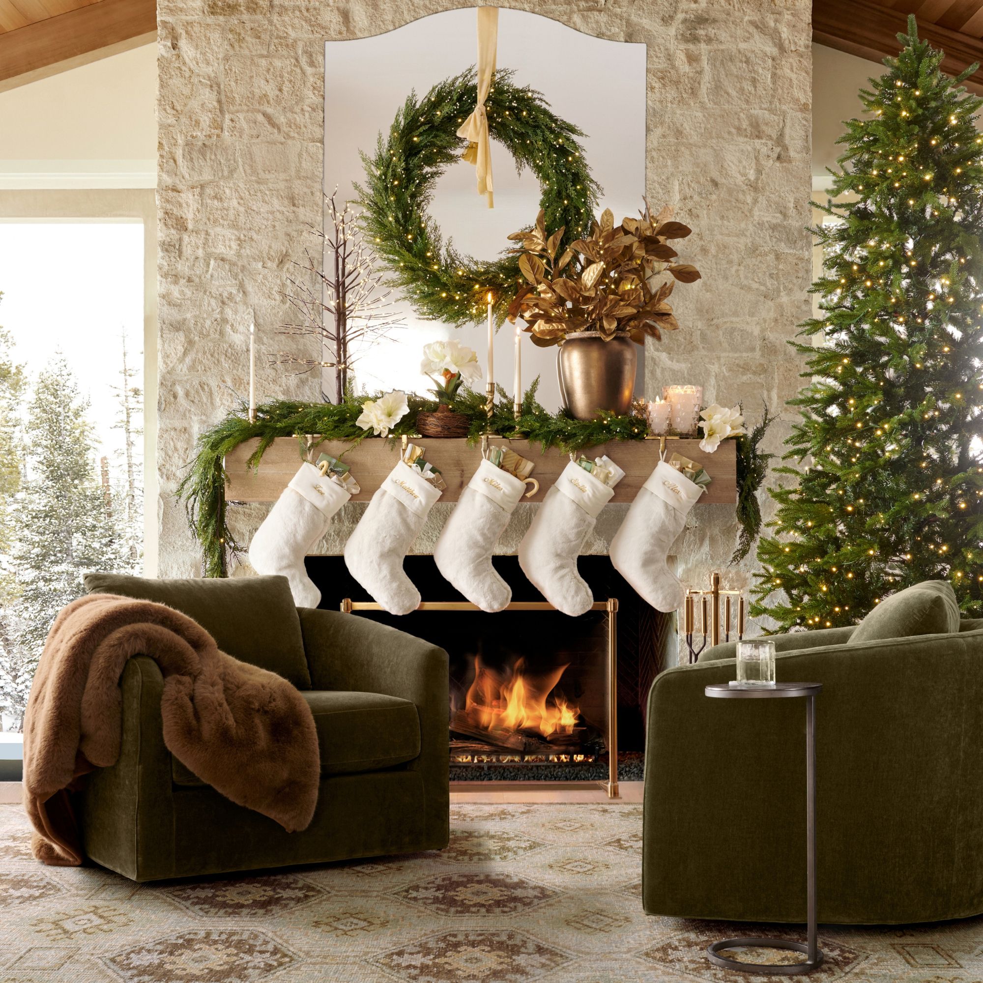 A large living room with a lit fire in the fireplace decorated with five stockings from the Pottery Barn Christmas collection