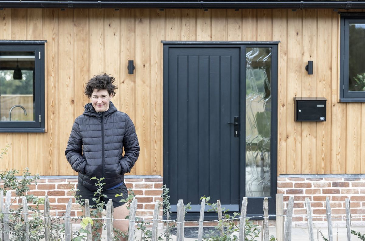 A woman stands outside a self-built oak frame home with her hands in her coat pockets