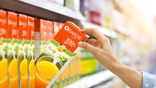 Person grabs for a carton of 100% fruit juice in the supermarket fridge aisle