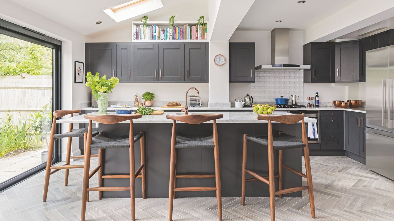 Large kitchen with a kitchen island surrounded by bar stools with grey cabinetry