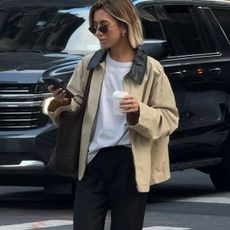 woman in barn jacket, t-shirt, and black pants looking at a phone