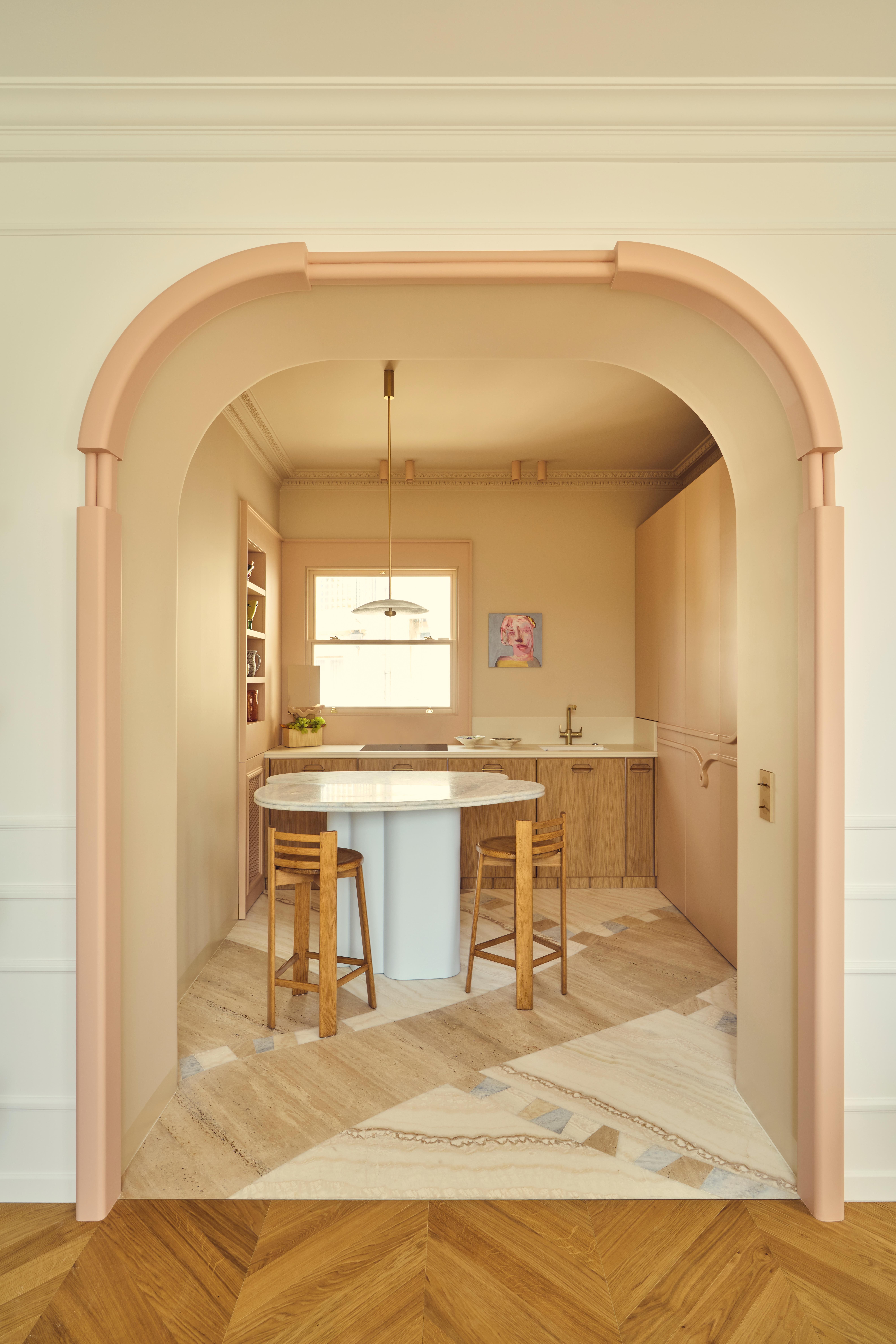 Batiik Studio-designed kitchen area featuring a rounded peach-lined archway, a custom marble dining table, Scandi-style low-back stools, and a pendant light overhead.