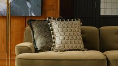 close up of patterned cushions on green sofa with timber wall panelling and artwork behind