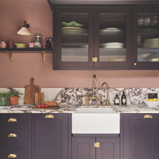 White Belfast sink with gold hardware in a purple and pink kitchen.