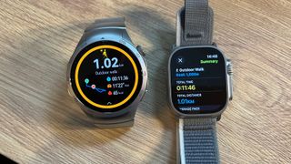 Huawei Watch GT 4 ja Apple Watch Ultra 2 vierekkäin puisella alustalla