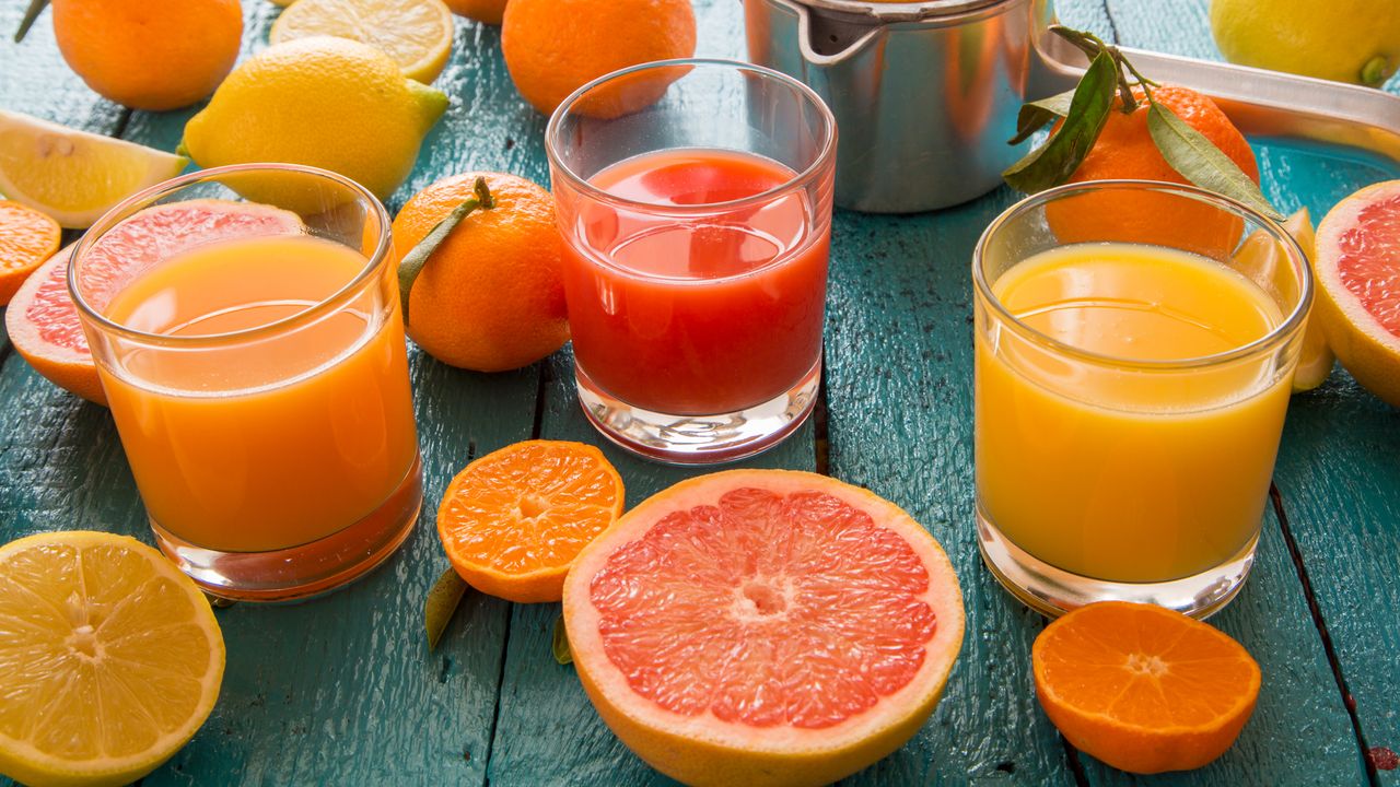 Table full of cut up oranges next to glasses of freshly squeezed orange juice