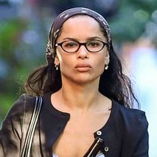 Zoe Kravitz wearing a black cardigan, white tank top, black pants, and black flats