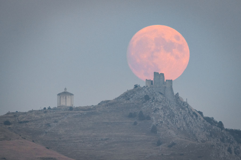 Luna llena de cosecha saliendo detrás de un castillo y una iglesia