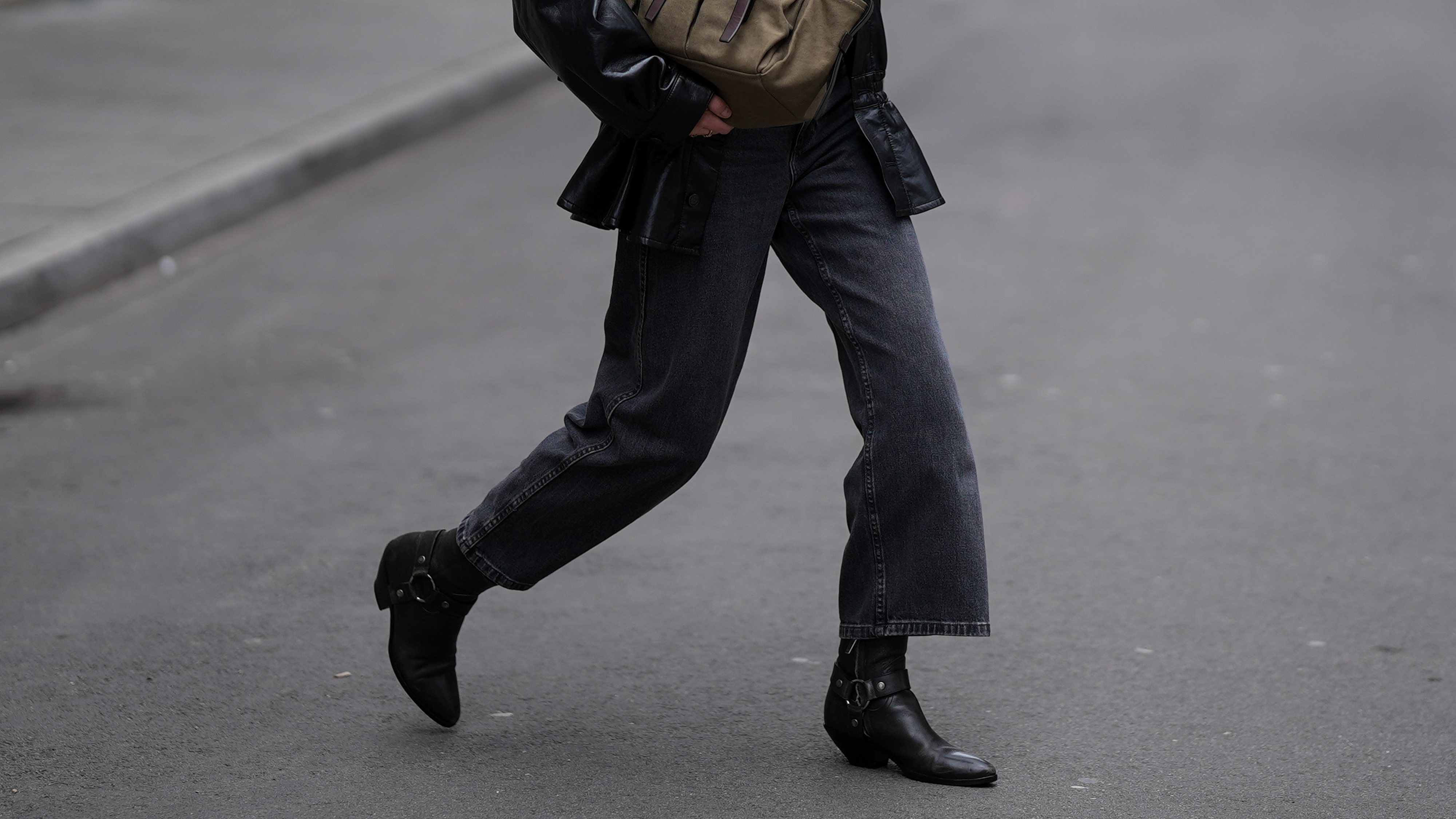 Photo of a woman wearing black jeans, black ankle boots, black jacket, white t-shirt, and sunglasses holding an olive bag.