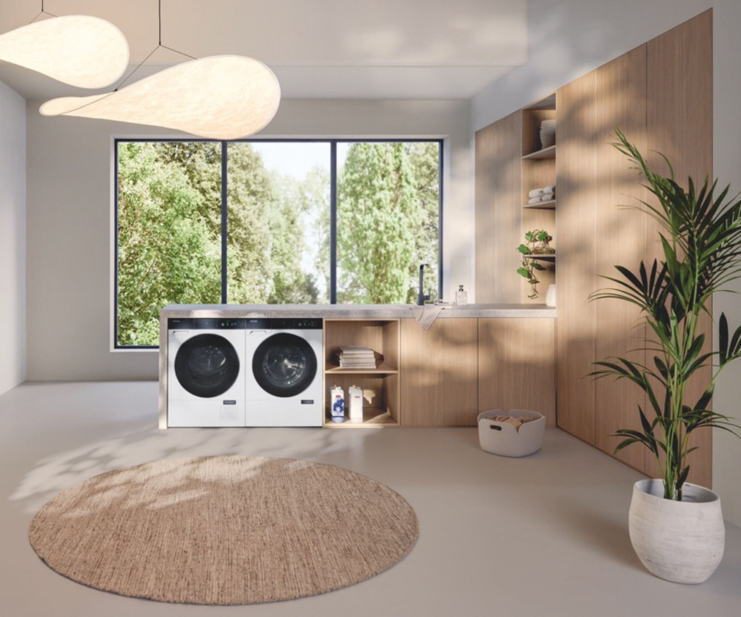 A modern laundry room features two white front-loading washing machines side by side, set into light wooden cabinetry with a grey stone countertop.