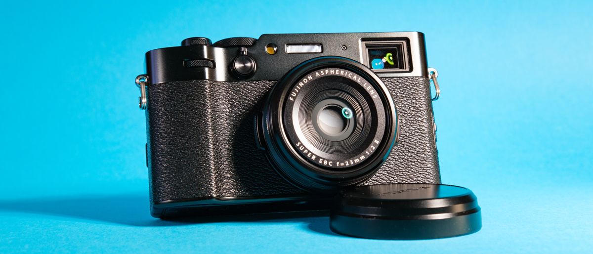 The Fujifilm X100VI mirrorless camera against a blue background propped up using the lens cap.