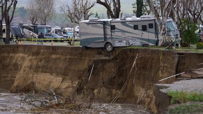 An RV balances on the edge of a river embankment that's about to give way because of flooding.