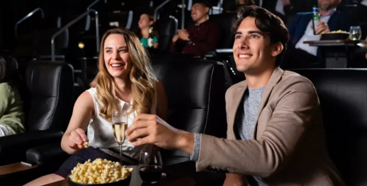 Man and woman sitting in movie theatre seats eating popcorn and holding champagne