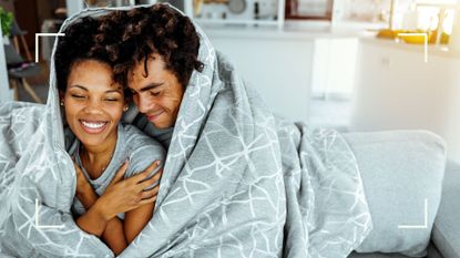 Man and woman bundled up in comforter on couch laughing and smiling, representing the reverse scoop sex position