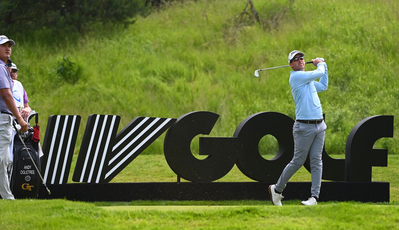 Andy Ogletree strikes an iron shot in front of a LIV Golf banner