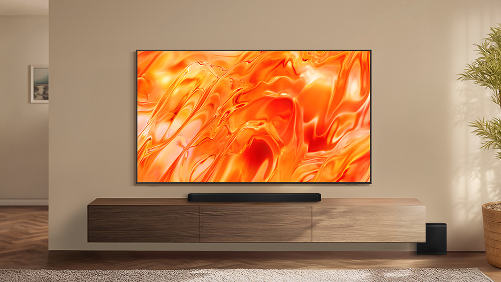 The Samsung QN70H Neo QLED TV displaying orange-colored, abstract imagery from a wall-mounted position in a well-lit, contemporary living space
