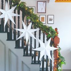 A hallway with a staircase with the railing decorated with a Christmas garland and star-shaped paper lanterns from IKEA