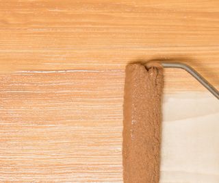 Small paint roller applying paint to wooden kitchen countertop