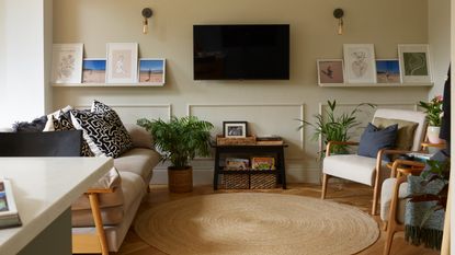 A living room with a TV hanging on the wall in the middle of the space with a round jute rug in the centre and a sofa and two matching chairs on either side