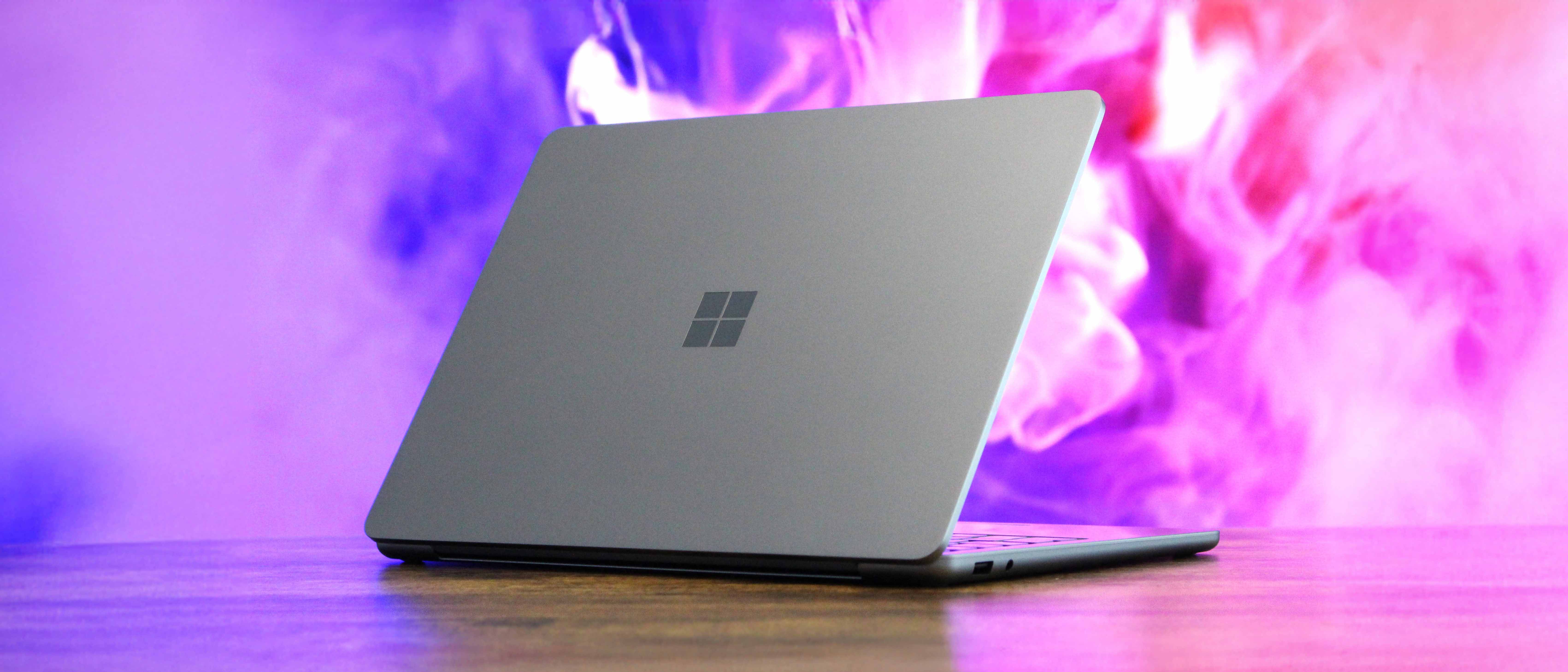 Surface Laptop 13-inch partly open on a wooden table in front of an abstract background.